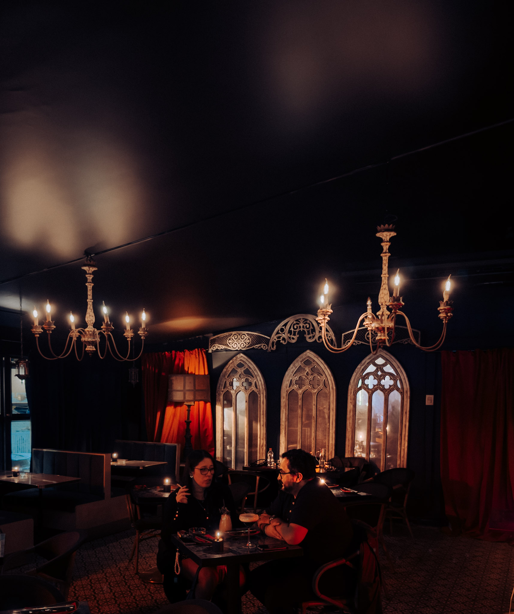Salón Gótico de Enigma, con arcos ojivales, cortinas rojas de terciopelo y lámparas góticas